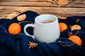 Big white cup of cocoa on the blue knitted sweater with vibrant orange tangerines and anise seeds around at wooden background Royalty Free Stock Photo