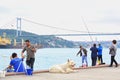 Big white dog on embankment with fishermen and Istanbul Bosphorus bridge background