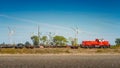 Big wind turbines to generate electrical power, green ecofriendly energy at blue sky with red cargo train going by at warm sunset Royalty Free Stock Photo