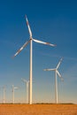 Big wind turbines to generate electrical power, green ecofriendly energy at blue sky standing in arid lifeless soil in warm sunset Royalty Free Stock Photo