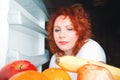 Big woman eat fruit. Red hair fat girl looking inside refrigerator. Unhealthy and healthy food concept with plus size female on k Royalty Free Stock Photo