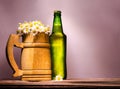 wooden beer mug with fine daisies similar to foam and a green full bottle with a metal lid Royalty Free Stock Photo