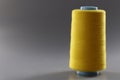 Big yellow bobbin of thin threads on a gray background