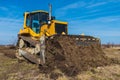 A big yellow bulldozer pushes the ground and makes a new road