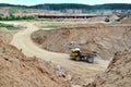 Big yellow dump truck transporting sand in an open-pit mining quarry.