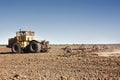 Big yellow tractor equipped with harrow working on the field