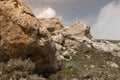 Big yellow weathered stone rock with lichen, cracks and dim green meadow in sunlight with fluffy white clouds in blue sky Royalty Free Stock Photo