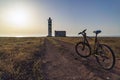 The bike stands on the road in front of the old lighthouse on the seashore, in the rays of the setting sun