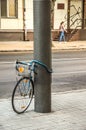 Bike tied to a post. In the background a walking woman