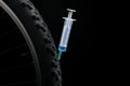 Bike wheel with syringe on black background, closeup. Using doping in cycling sport concept Royalty Free Stock Photo