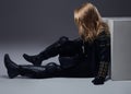 Fashion, sport, extreme. Biker girl wearing leather racer costume sitting on a floor in a studio. Royalty Free Stock Photo