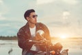 Biker man standing smokes with his motorbike beside the natural lake and beautiful, enjoying freedom and active lifestyle, having