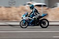 Biker ride Suzuki motorcycle on the city road with motion blurred background. Motorcyclist in cyan helmet and jacket on blue