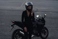 Biker woman in black leather jacket and full face helmet sits near stylish sports motorcycle at urban parking. Traveling Royalty Free Stock Photo