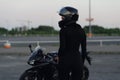 Biker woman in black leather jacket and full face helmet sits near stylish sports motorcycle at urban parking. Traveling Royalty Free Stock Photo