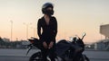 Biker woman in black leather jacket and full face helmet sits near stylish sports motorcycle at urban parking. Traveling Royalty Free Stock Photo