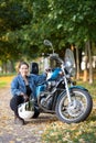 Biker woman with white helmet and jeans outfit portrait, sitting close to motorbike, autumn park Royalty Free Stock Photo
