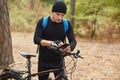 Bikers using smart phone gps application to find right way in forest, attractive guy stops on road in wood, rider wears black