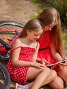 Bikes cycling girl into park. Children watch tablet pc. Royalty Free Stock Photo