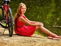 Bikes cycling girl into park. Girl sits leaning on bicycle on shore. Royalty Free Stock Photo