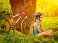 Bikes cycling girl wearing helmet have rest sitting under tree. Royalty Free Stock Photo