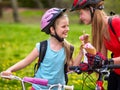 Bikes cycling girls with rucksack cycling eating ice cream cone in summer park. Royalty Free Stock Photo