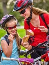 Bikes cycling girls with rucksack cycling eating ice cream cone in summer park. Royalty Free Stock Photo