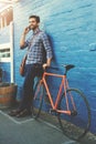 Bikes take you there and cellphones show you where. a handsome young man posing with his bicycle against a blue wall.