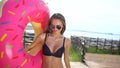 Bikini girl walking with sprinkled donut float at pool in sun day. Party, hotel, beach, holiday, vacation, travel