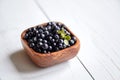 Bilberries with green leaf into a bowl on white wooden background, many fresh dark blue berries on table Royalty Free Stock Photo