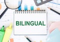 BILINGUAL text on white paper with office tools on office background Royalty Free Stock Photo