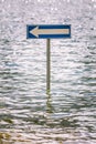 Billboard road arrow to the left partially submerged by flood water.