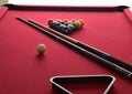 Billiard balls on a red pool table with two cues, a black ball rack and a white cue ball