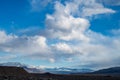 Billowy white clouds in blue sky over snowy mountain shrouded in clouds Royalty Free Stock Photo