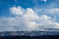 Billowy white clouds in blue sky over snowy mountain shrouded in clouds Royalty Free Stock Photo