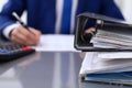 Binders with papers are waiting to be processed with businessman back in blur. Accounting planning budget, audit