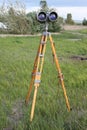 A binoculars with a tripod with a azimuth head in a forest on a sand with grass