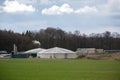 Biogas plant with straw bale stock and smoking chimney on the field at the edge of the forest, cloudy sky, copy space