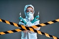 Biological hazard. Epidemic of the Chinese coronavirus. Woman in a protective suit and mask holds an injection syringe and vaccine