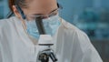 Biologist with face mask using microscope to work on experiment Royalty Free Stock Photo