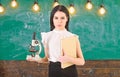 Biology concept. Lady in formal wear on calm face in classroom. Lady scientist holds book and microscope, chalkboard on Royalty Free Stock Photo