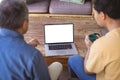 Biracial adult son and senior father holding cups of coffe and making laptop video call Royalty Free Stock Photo