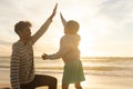 Biracial boy giving high-five to smiling father kneeling at beach against sky during sunset Royalty Free Stock Photo