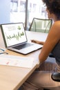 Biracial businesswoman analyzing infographic business report over laptop on desk at office