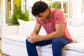Biracial depressed young man with hands clasped sitting on sofa in living room, copy space Royalty Free Stock Photo