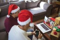 Biracial father and adult son making laptop christmas video call with waving female friend Royalty Free Stock Photo