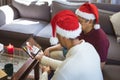 Biracial father and son in santa hats making tablet christmas video call with waving woman Royalty Free Stock Photo