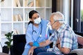 Biracial female doctor examining caucasian senior man wearing oxygen mask sitting on sofa at home