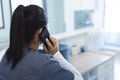 Biracial female doctor talking on smartphone at reception desk in hospital, copy space Royalty Free Stock Photo