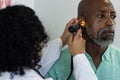 Biracial female doctor using otoscopy and examinating african american male patient